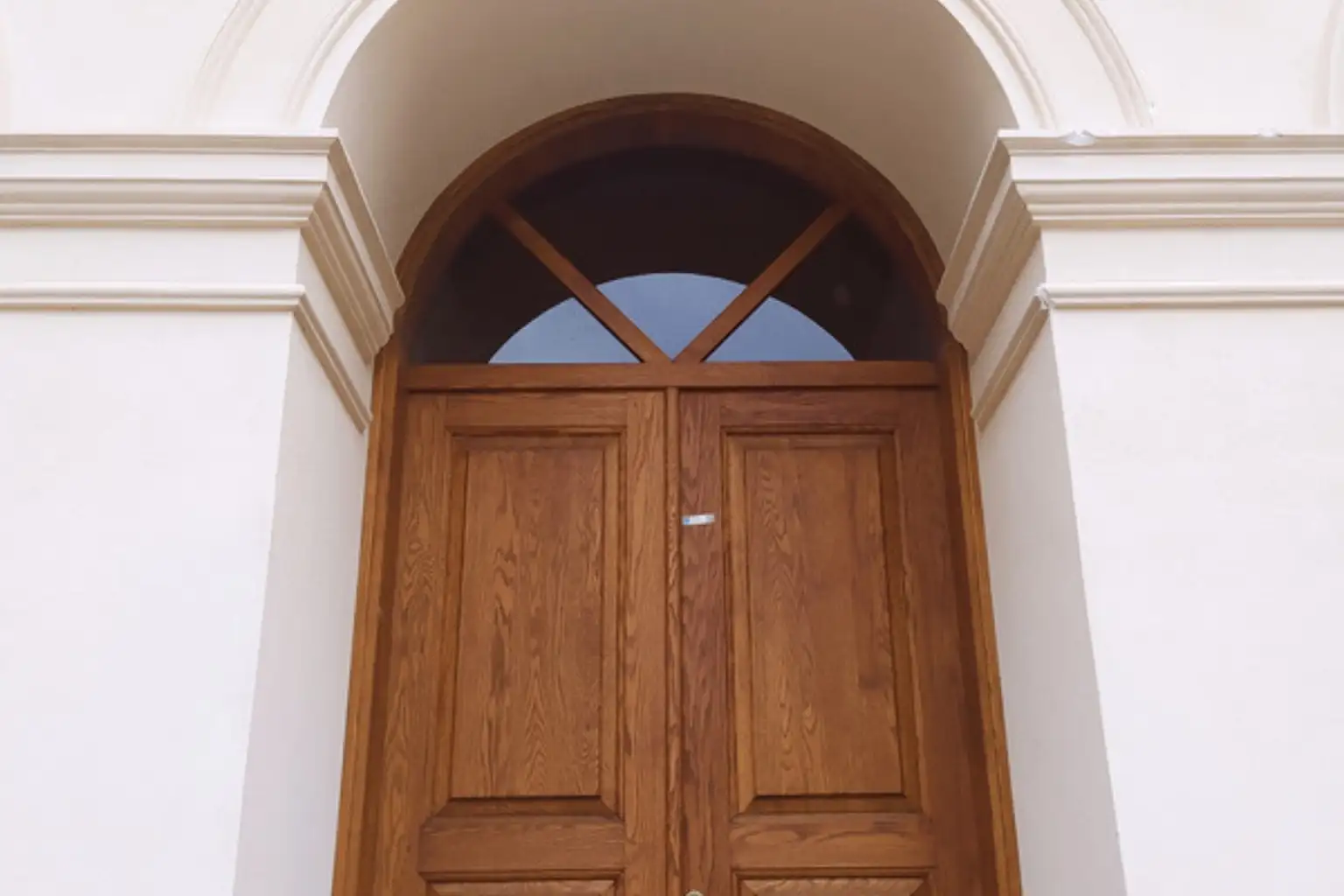 Hoveddør i træ med rundbue og glas foroven i en lys facade